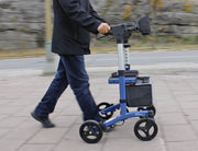 Person using a blue knee walker on a paved path with a blurred background