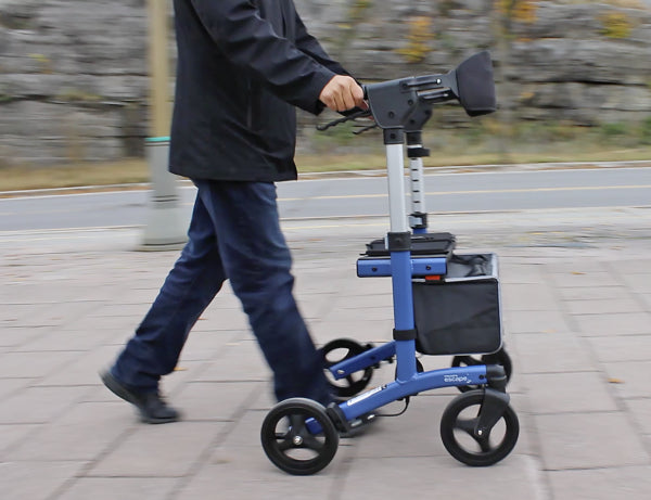 Person using a blue knee walker on a paved path with a blurred background