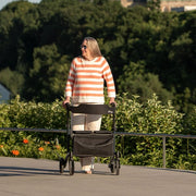 Person pushing a stroller on a path with greenery in the background