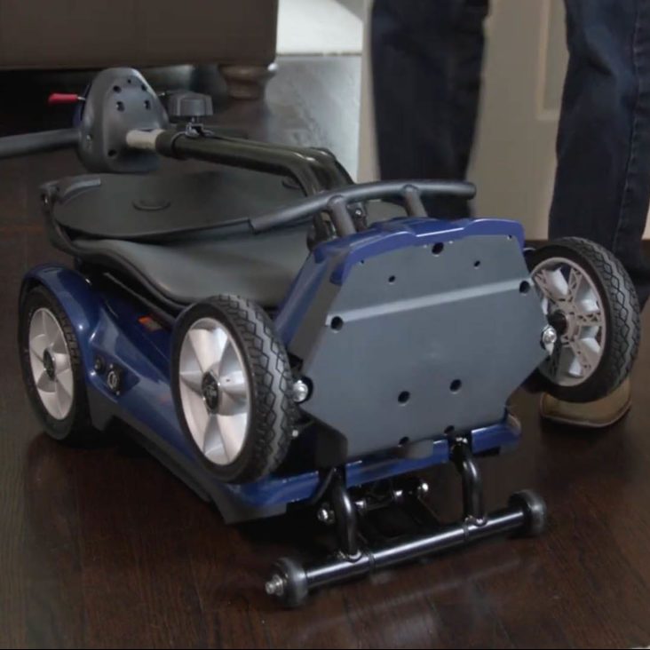 Blue and black mobility scooter on a wooden floor with a person partially visible.