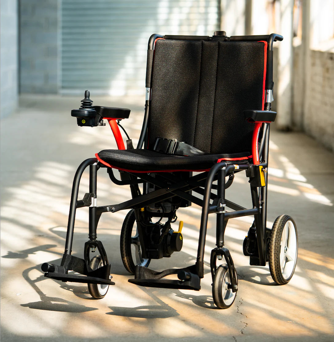 Black and red electric wheelchair on a wooden floor with sunlight casting shadows.