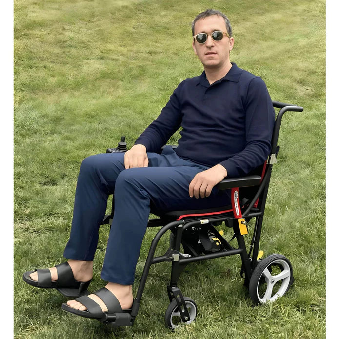 Man in a wheelchair sitting on grass wearing sunglasses and a navy outfit.