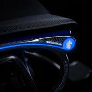 Close-up of a carbon-fiber armrest with a glowing blue LED light strip and a circular blue logo featuring a white horse head, set against a dark interior background.