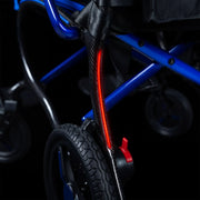Close-up of a wheelchair frame with a bright red illuminated safety light mounted on a black carbon-fiber-style vertical bar, set against a dark background.