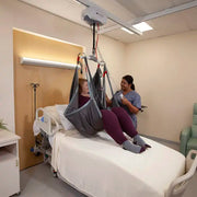Person using a patient lift in a hospital room with another person assisting.