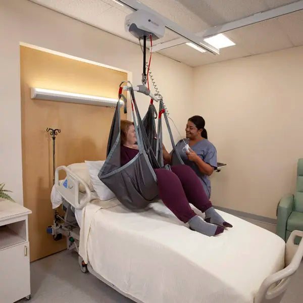 Person using a patient lift in a hospital room with another person assisting.