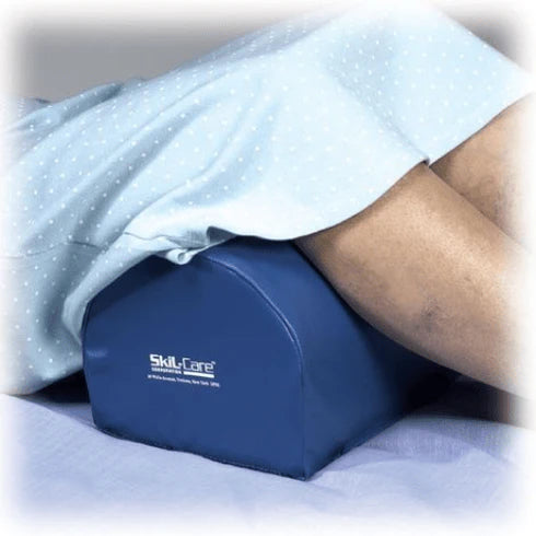Blue Skil-Care pillow under a person lying in bed with white sheets.