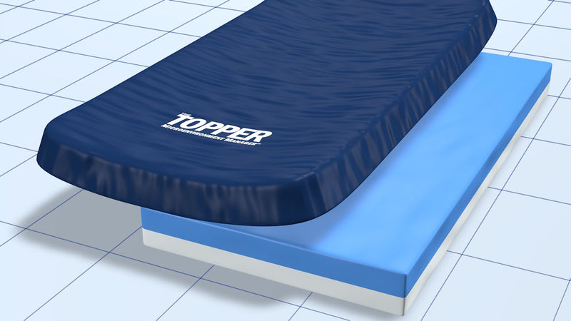 A navy blue TOPPER brand mattress topper shown partially lifted over a light blue mattress base on a white and gray tiled floor background.