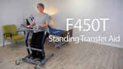 A woman using an F450T standing transfer aid in a bright room with wood floors, a green chair, and a treatment table. Large white text on the right reads 'F450T Standing Transfer Aid'.