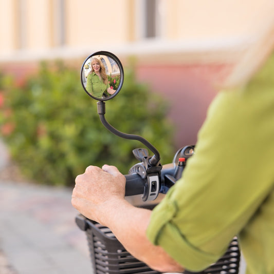 Person riding a bike with a round mirror attached to the handlebar, reflecting a person taking a photo.