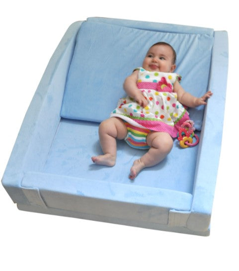 Baby sitting on a blue changing table with a colorful dress and toy.