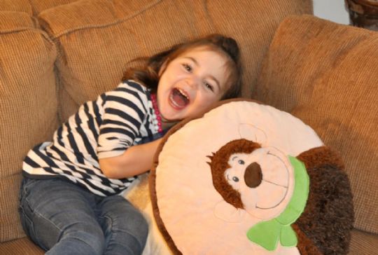 Child lying on a brown couch with a large hedgehog-shaped pillow