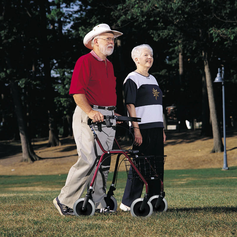 An older man wearing a white cowboy hat uses a four-wheel walker with a basket in a park, accompanied by an older woman in a black, white, and gray top.