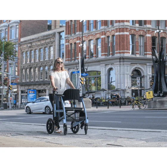 Woman pushing a rollator on a city street with buildings and traffic lights in the background.