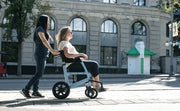Two women using a mobility scooter on a city street.