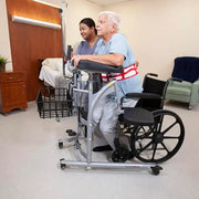 Person using a walker in a medical setting with another person assisting.