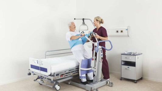 Person using a hospital lift in a medical setting with a nurse assisting.