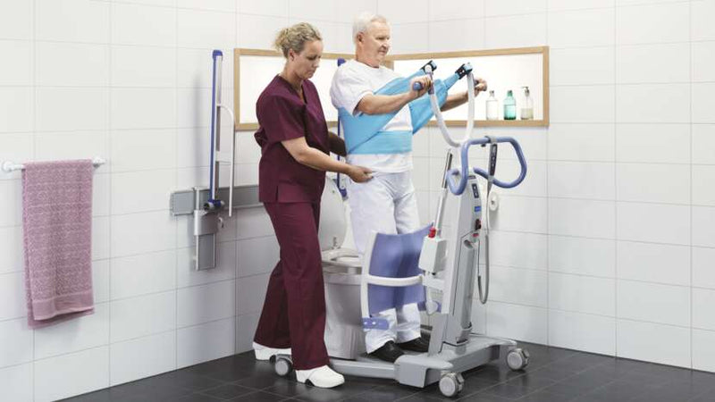 Person using a medical device with another person assisting in a bathroom setting.