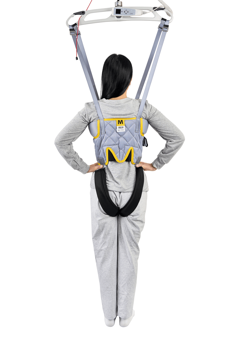 A person viewed from behind wearing a gray and yellow back support harness with a black waist belt, suspended from a white overhead frame against a white background.
