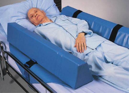Person lying in a hospital bed with a blue safety rail.