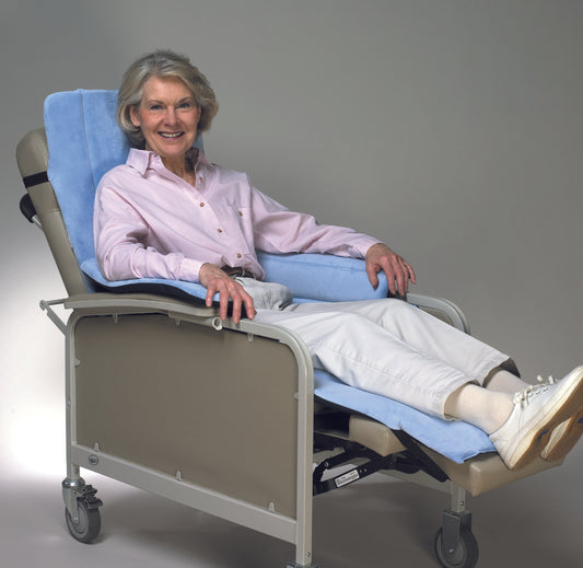 Woman sitting in a hospital bed with a blue pillow and white sheets on a gray background