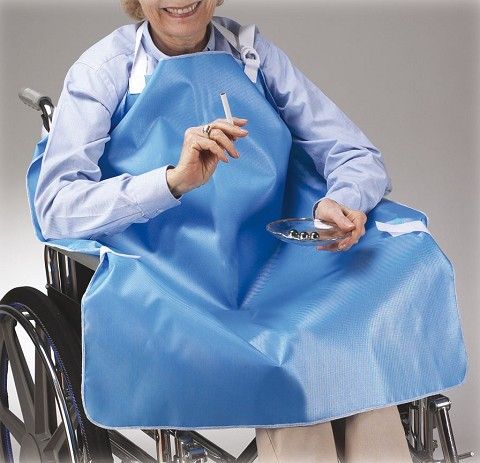 Person in a wheelchair wearing a blue apron, holding a cigarette and a plate.