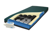 An electric mattress pad shown in a cross-section view on a white background, featuring a dark green top layer, blue and beige layers, four black and silver air pockets labeled PressureGuard APW, and a white handheld controller with a blue digital display. The brand 'SDAN' is visible on the controller.